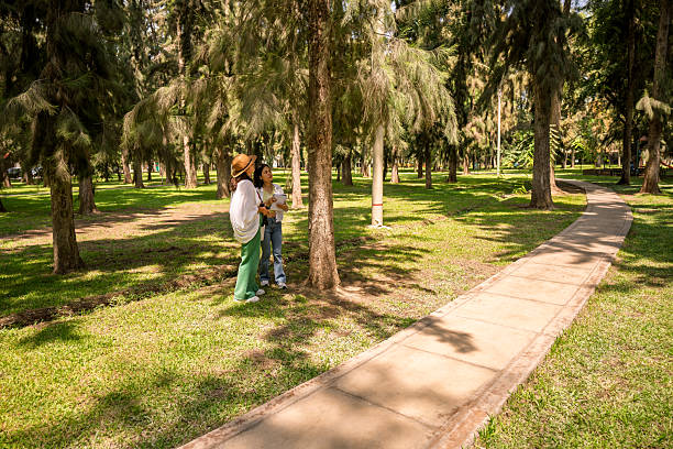 Two young adult female biology students doing botanical fieldwork, observing trees and plants in a sunny urban park