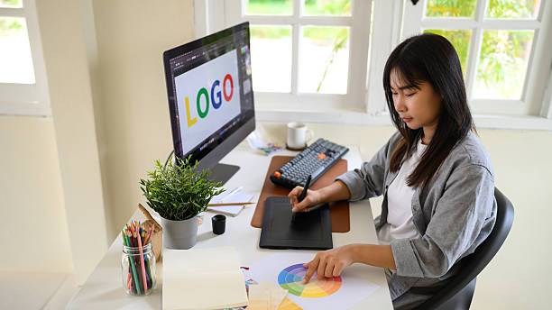 istock Graphic designer creating logo on digital tablet in bright modern workspace with computer and color palette 2241024618