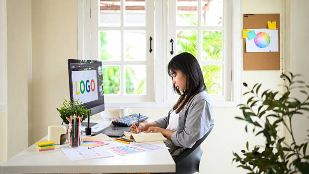 istock Creative woman designing logo sketches on notebook with color samples and tools in bright modern workspace 2241024662