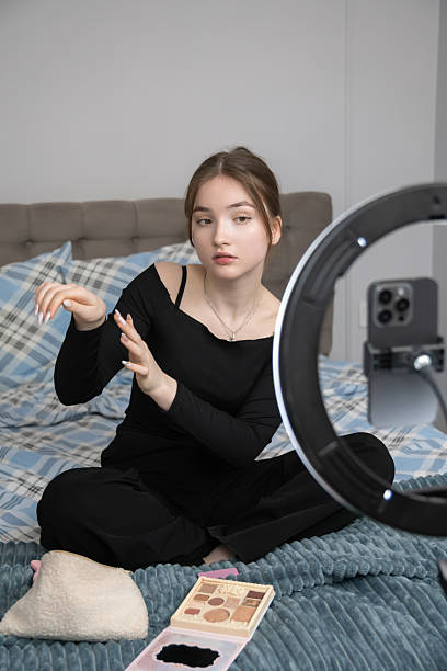 istock Teenager beauty blogger recording a makeup tutorial video on a smartphone, showcasing various cosmetics products under the glow of a ring lamp in her cozy bedroom 2241027504