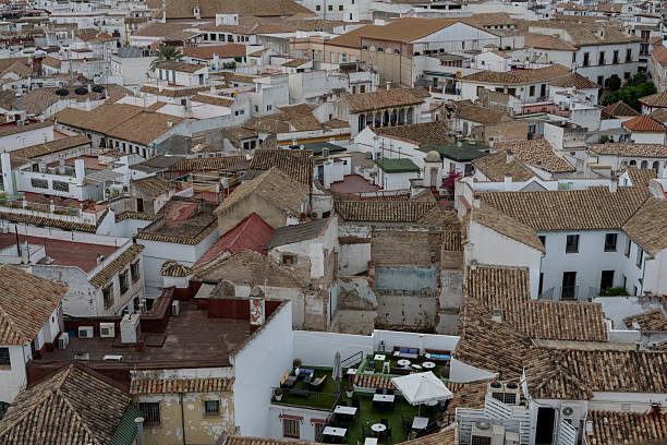 A picturesque glimpse of Cordoba's white and red rooftops, with the city's skyline in the background. The image captures traditional Andalusian architecture, narrow streets, and the unique atmosphere of this historic Spanish city.