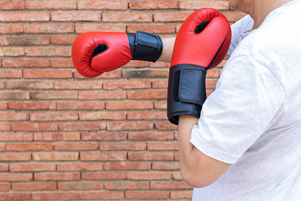 Person is wearing red boxing gloves, practicing punches and defensive moves during a workout session against a textured brick wall, focusing on fitness and self-improvement