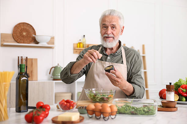 istock Elderly man cooking salad at white marble table in kitchen 2241036212