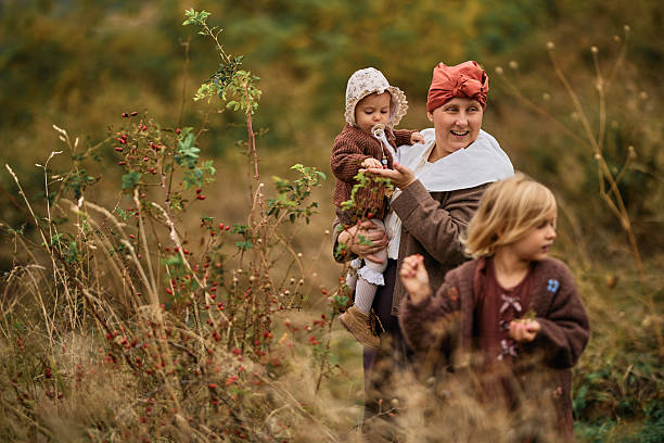 Mother holding baby and walking with daughter in an autumn field, picking berries. Family enjoying nature