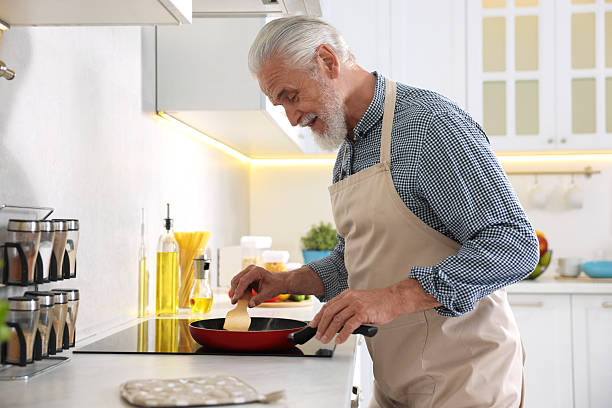 istock Elderly man cooking dish on cooktop in kitchen 2241036339
