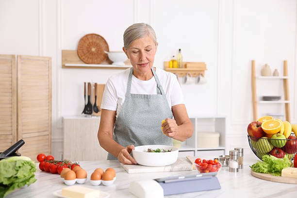 istock Senior woman cooking salad at white marble table in kitchen 2241036467