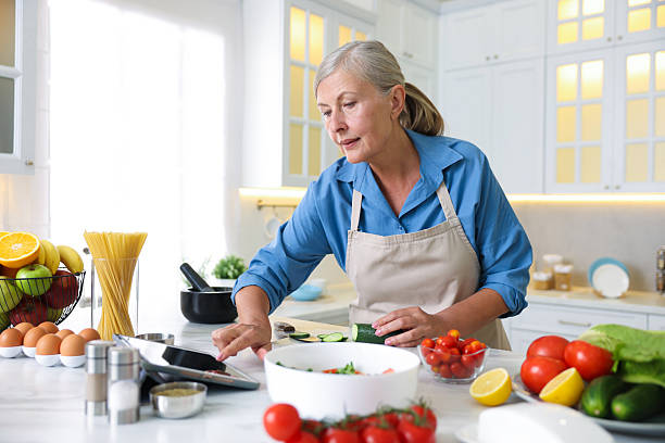 istock Senior woman using tablet while cooking at white marble table in kitchen 2241046462