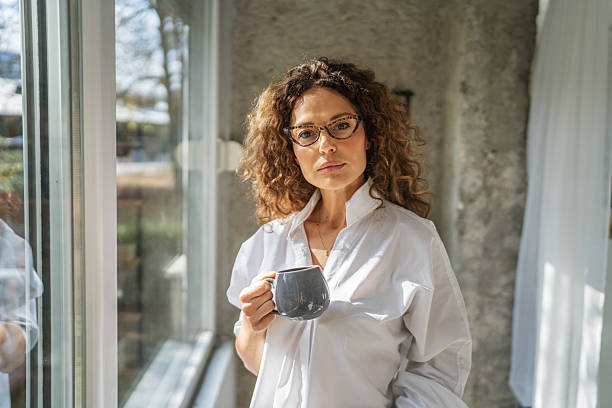 istock Woman drinking coffee by window thoughtfully starting new day 2241047324