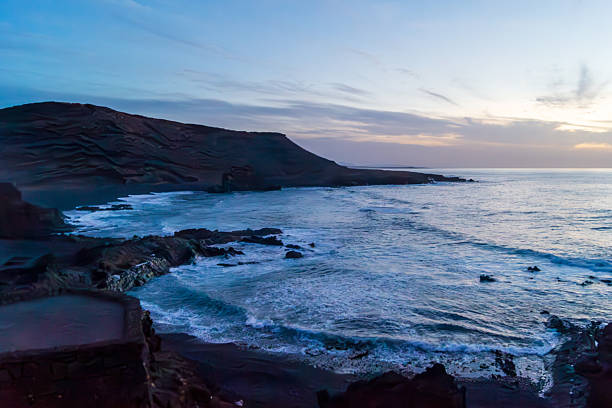 Golden hour colors the sky and the Atlantic coastline at El Golfo, Lanzarote. The volcanic rocks and soft waves highlight an idyllic, natural scene ideal for travel, leisure, and sunset lovers.