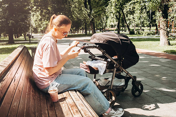 istock Young mom enjoys summer day in a park, sitting on a bench with a stroller, while drinking a refreshing cocktail and using her phone. Relaxed and multitasking in nature. 2241049157