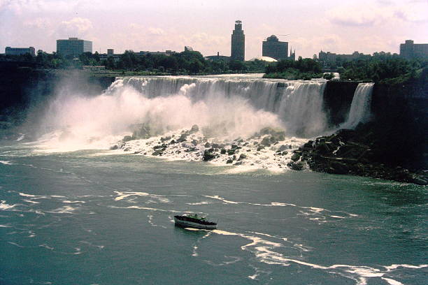 A vintage 1984 slide film image of Niagara Falls, capturing the iconic cascade in rich analog tones. The powerful rush of water plunges over the edge, framed by mist and softened by the warm color palette typical of film photography from the era. The scene evokes both the timeless force of nature and the nostalgic texture of mid-1980s travel documentation