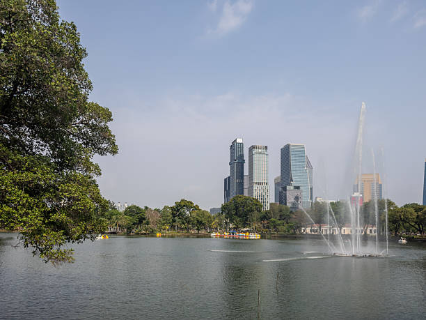 Lumphini Park, Bangkok, captures urban tranquility. Modern skyscrapers and lush trees frame a serene lake with refreshing fountains, showcasing a harmonious blend of nature and contemporary city