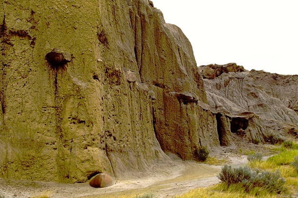 A 1985 slide film image of the South Dakota Badlands, capturing the rugged terrain in warm, analog hues. Jagged rock formations rise from the arid landscape, their striated layers revealing millennia of erosion and sediment. The vintage film grain adds nostalgic depth to the stark beauty of the scene, evoking a timeless sense of isolation, resilience, and geological wonder.