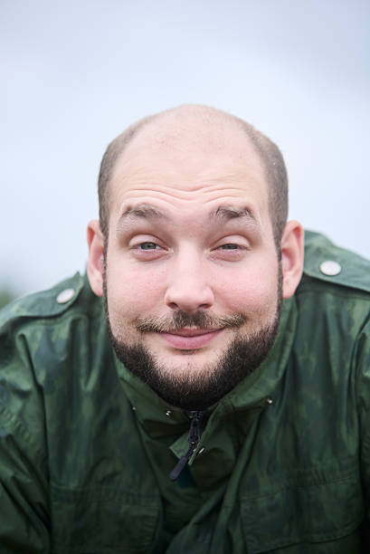 Portrait of a young man looking at the camera with sleepy smile. He is outdoors and his jacket is wet from the recent rain.