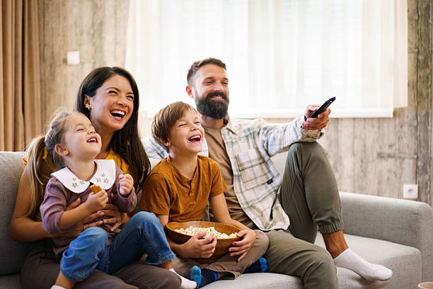 istock Family laughing on couch watching television together 2241069007