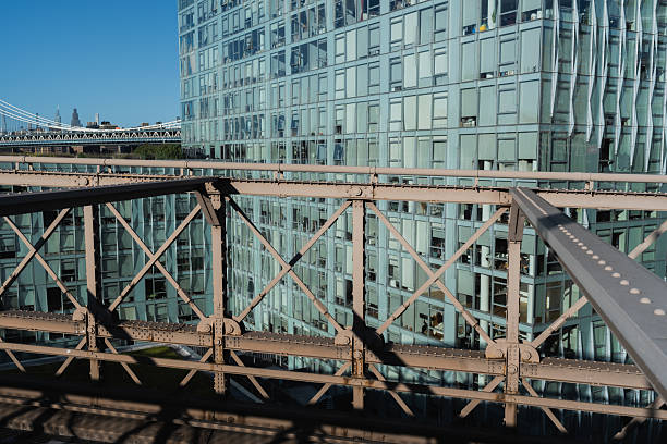 Framing manhattan bridge with industrial bridge architecture and a contemporary glass building against a clear blue sky