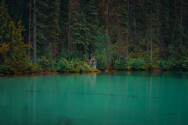 Emerald lake with figures at a viewing platform surrounded by a green forest. Radium Hot Springs, BC