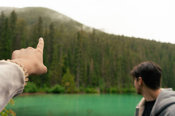 Pointing to a scenic forest and lake view with lush, green trees. Radium Hot Springs, BC