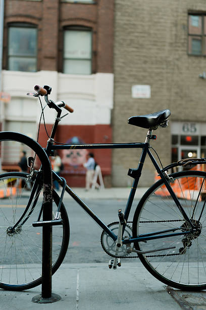Vintage bicycle securely locked to a metal pole on a sidewalk in an urban setting, with buildings in the background