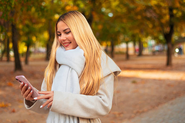 istock Beautiful smiling young woman using phone while spending time in the autumn nature 2241073210