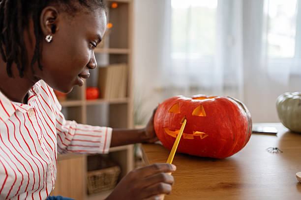 A dedicated young black woman creates a jack-o’-lantern while decorating for Halloween at home