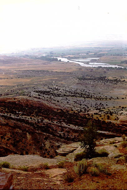 A 1986 slide film image of Colorado National Monument, showcasing dramatic sandstone monoliths rising from the arid canyon floor. The towering spires and layered rock formations are etched with striations shaped by millennia of erosion, glowing in warm analog tones beneath a partly cloudy sky. The vintage film grain adds nostalgic depth to the rugged grandeur, evoking the spirit of mid-80s travel and the timeless power of the American Southwest.