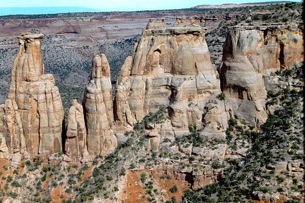 A 1986 slide film image of Colorado National Monument, showcasing dramatic sandstone monoliths rising from the arid canyon floor. The towering spires and layered rock formations are etched with striations shaped by millennia of erosion, glowing in warm analog tones beneath a partly cloudy sky. The vintage film grain adds nostalgic depth to the rugged grandeur, evoking the spirit of mid-80s travel and the timeless power of the American Southwest.