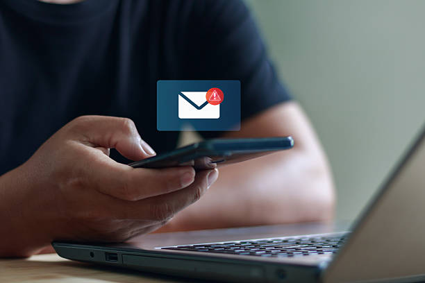 istock Businessman using smartphone and laptop with new email notification icon, representing online communication, digital messaging, mobile technology and internet connection in modern lifestyle. 2241087072