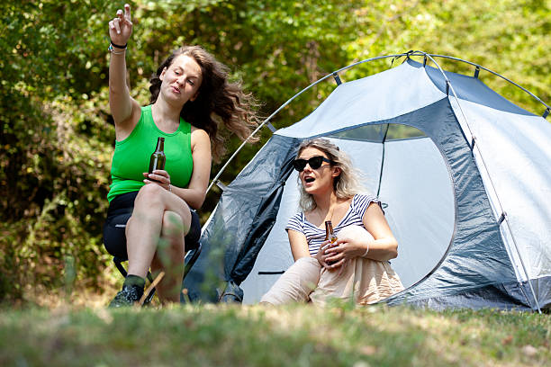 istock Two women relax in nature during a camping trip, sharing drinks and laughter. One gestures animatedly while the other smiles, both enjoying the peaceful outdoor atmosphere 2241090148