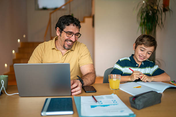istock Hispanic Father Engages in Remote Work While Assisting Happy Son with Homework 2241091718