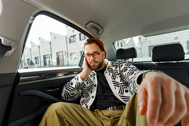 Cheerful young man in casual clothing sitting relaxed in the backseat of a car, smiling broadly and gesturing peace sign with his hand.