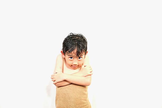 Adorable young boy wrapped in brown towel after bath, feeling chilly and shy while drying himself at home.