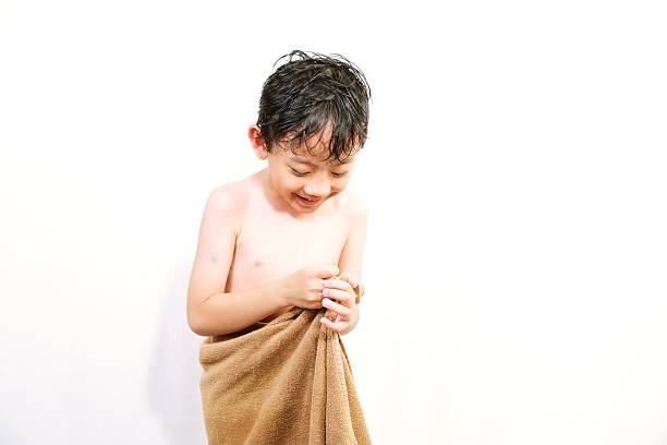 Sweet little boy wrapped in towel looking down after bath, showing shyness and innocence in natural light.