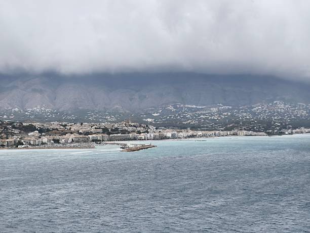An absolutely stunning coastal landscape that showcases a beautiful beach, majestic mountains, and a cloudy sky