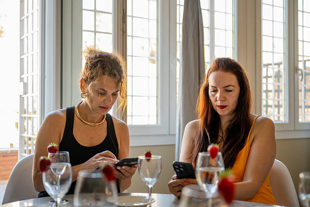 istock Two women sitting at table using smartphones indoors 2241102561