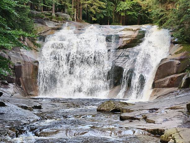 A breathtaking and stunning waterfall endlessly flows over a rocky terrain, surrounded by vibrant green trees