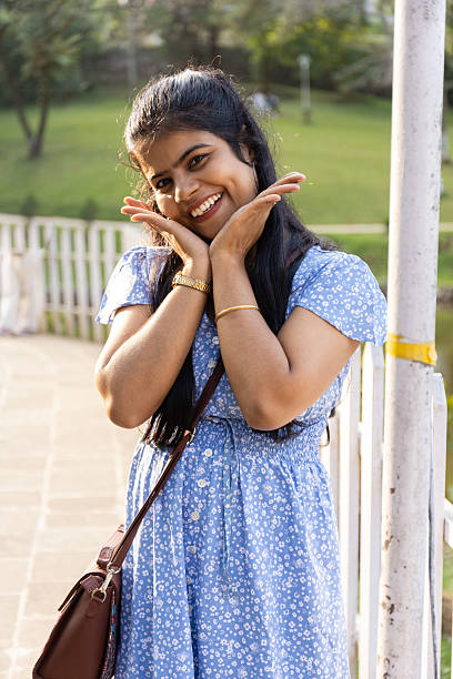 A pretty beautiful middle aged Indian female girl in blue dress smiling, standing outdoors in a park