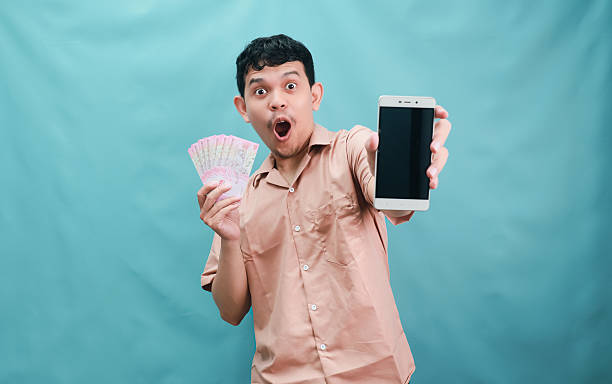 istock Excited man showcasing money and phone against a teal backdrop. 2241112230