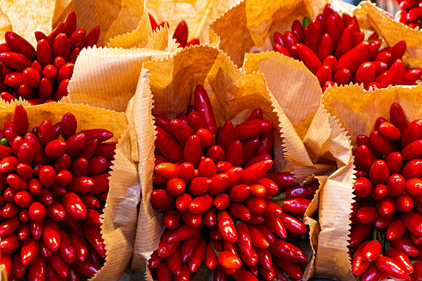 A vibrant display of bright orange and red chili peppers (gindillas) in a neon pink box at a vegetable stall in the historic Rialto Market in Venice, Italy.