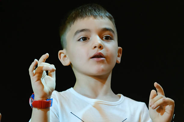 A young boy with a red wristband is making a peace sign with his hands. The boy is wearing a white shirt and he is in a relaxed and happy mood