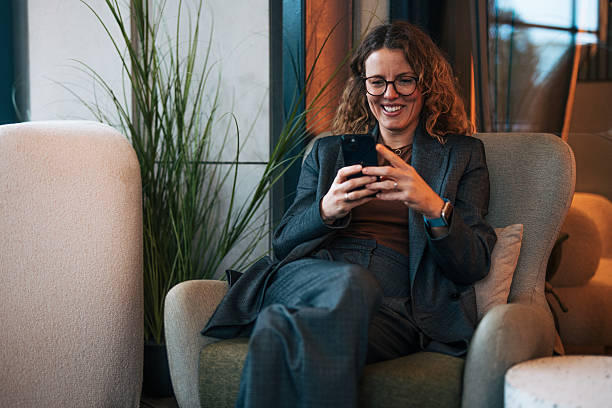 istock Professional woman using phone while relaxing in modern office lounge 2241131868