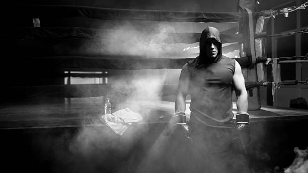 A shadowy silhouette of a boxer poised to strike against a backdrop of dramatic lighting creates a sense of anticipation and tension. The use of light enhances the atmosphere, symbolizing the focus and readiness required for success in competitive sports.