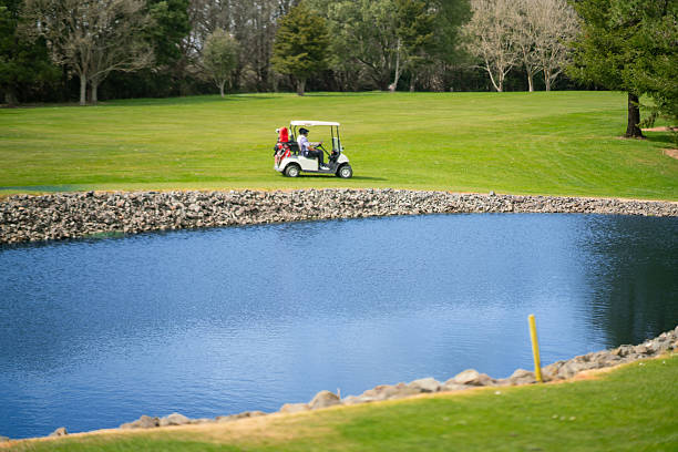 Golfers cruise through the vibrant fairways in their golf cart, enjoying a calm and cheerful ride amid the beautiful golf course landscape with water body front.
