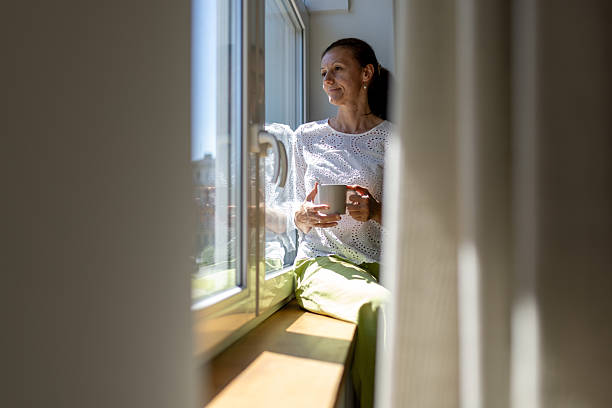 istock Woman sitting by the window, drinking coffee 2241138299