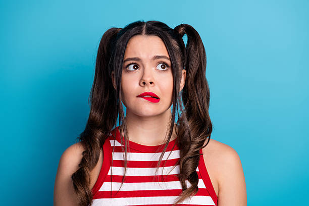 istock Young woman in a striped top with a curious expression, posing against a blue background, displaying fun and youthful energy. 2241139986