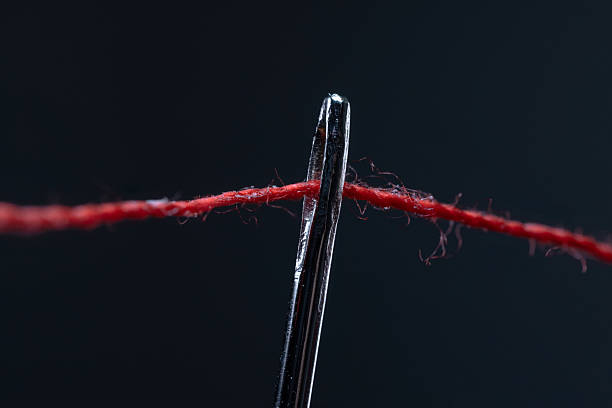 multi-colored threads for sewing in the form of a rainbow pass through an antique needle on a black background close-up