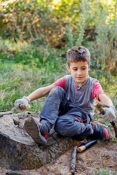 istock Boy wearing gloves holding branches in hands, sitting on a tree stump 2241141669