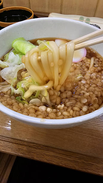 Traditional Japanese udon noodle soup with tempura bits, broth, cabbage, and fishcake and vegetables on a wooden table