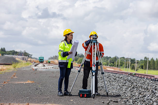 istock Two railway engineers wearing safety helmets and reflective jackets use a tripod surveying instrument to measure track alignment. The image represents teamwork, precision, and infrastructure development. 2241144164