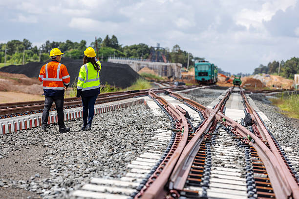 istock Two railway engineers wearing helmets and reflective jackets walk along new rail tracks under construction. The image represents teamwork, infrastructure development, and modern railway engineering. 2241144212